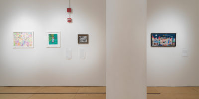 An installation photograph of 4 framed images mounted on the wall. The four images are smaller pieces under 11x17 inches. Three images on the left side are separated by the 4th image on the right by a circular pillar. The first image on the far left side is a drawing of pink, purple and blue pastel in various shapes. The second image is a drawing of a person with a blue and green background. The third image, the smallest of the bunch, is a black and white image with a dark frame. The far right, fourth image, is a colorful drawing of a city-scape in the evening. A full moon is in placed in the top left of the drawing.