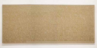 A photograph of a large canvas that is 9 feet wise and three feet tall. The canvas is a light brown color. In hand-written text, a paragraph in spanish language covers the entirety of the canvas. The hand-writing is written in a dark, tan color.