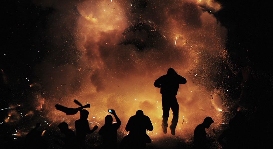 the photograph. They are looking towards the background, in which a large, orange firework is exploding.