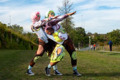 Two people sharing one costume stand in alignment with one arm up diagonally.