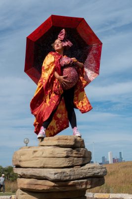 A person dressed in red with a red umbrella stands at the top of a rock.