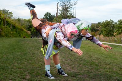 Two people with one leg each in a single pant leg both lift their other leg high into the air behind them.