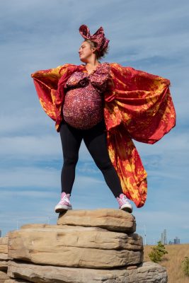 A person dressed in red stands with their arms outstretched at the top of a rock.