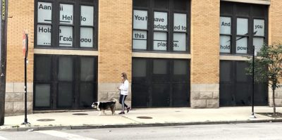 Light brick building with windows lined with white paper with black text. Text reads 