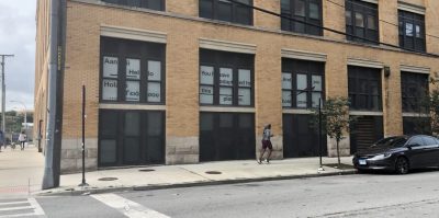 Light brick building with windows lined with white paper with black text. Text reads 