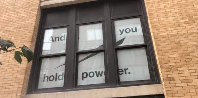 Close up of a window covered in white paper with black text reading, 