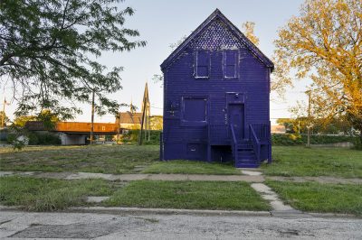 Blue house surrounded by grass and a concrete sidewalk.