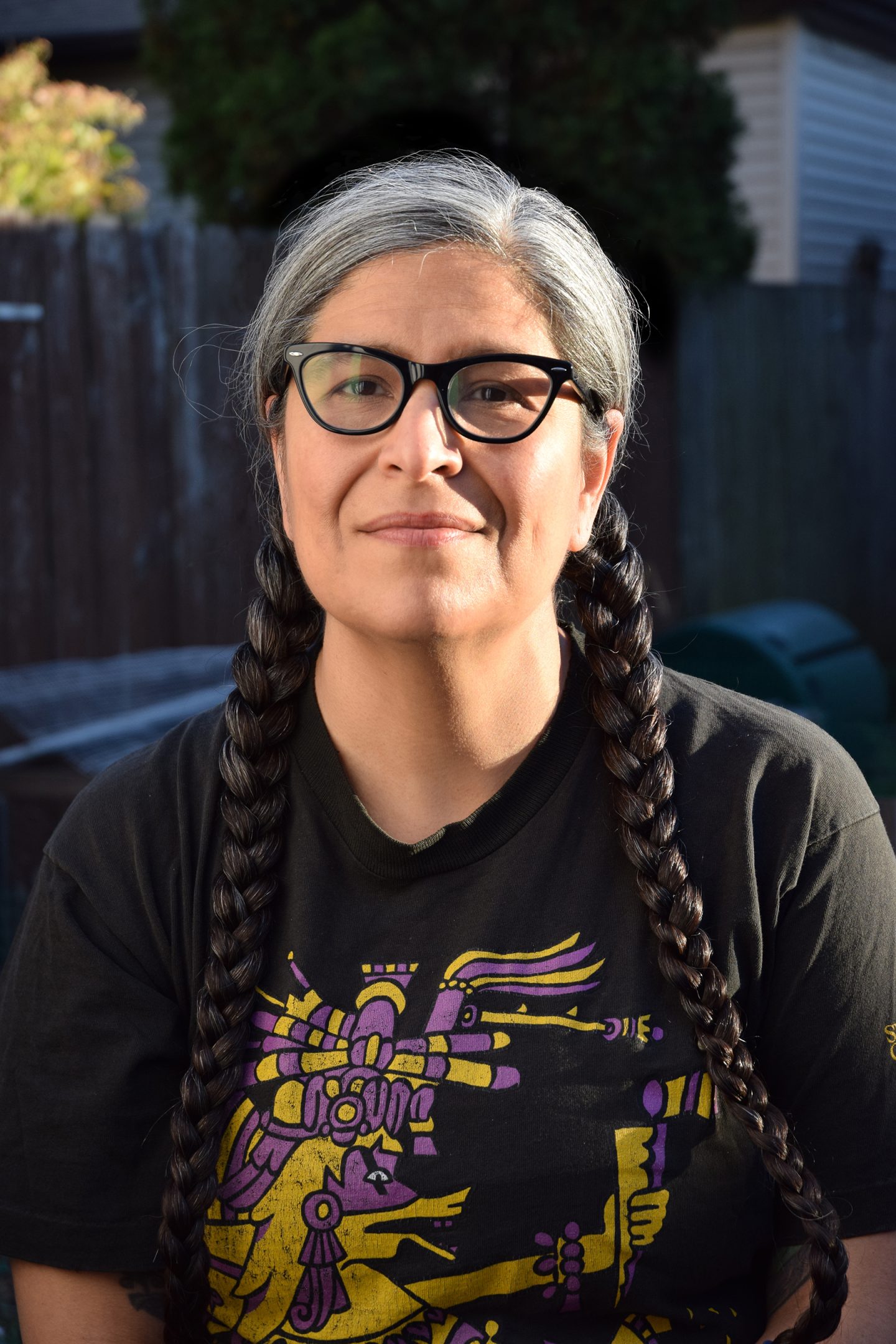 Headshot of a medium-skinned woman with glasses and long grew and black hair in two braids.