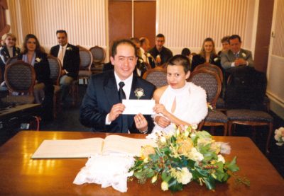 Couple sitting in a room holding a card with people sitting in the background.